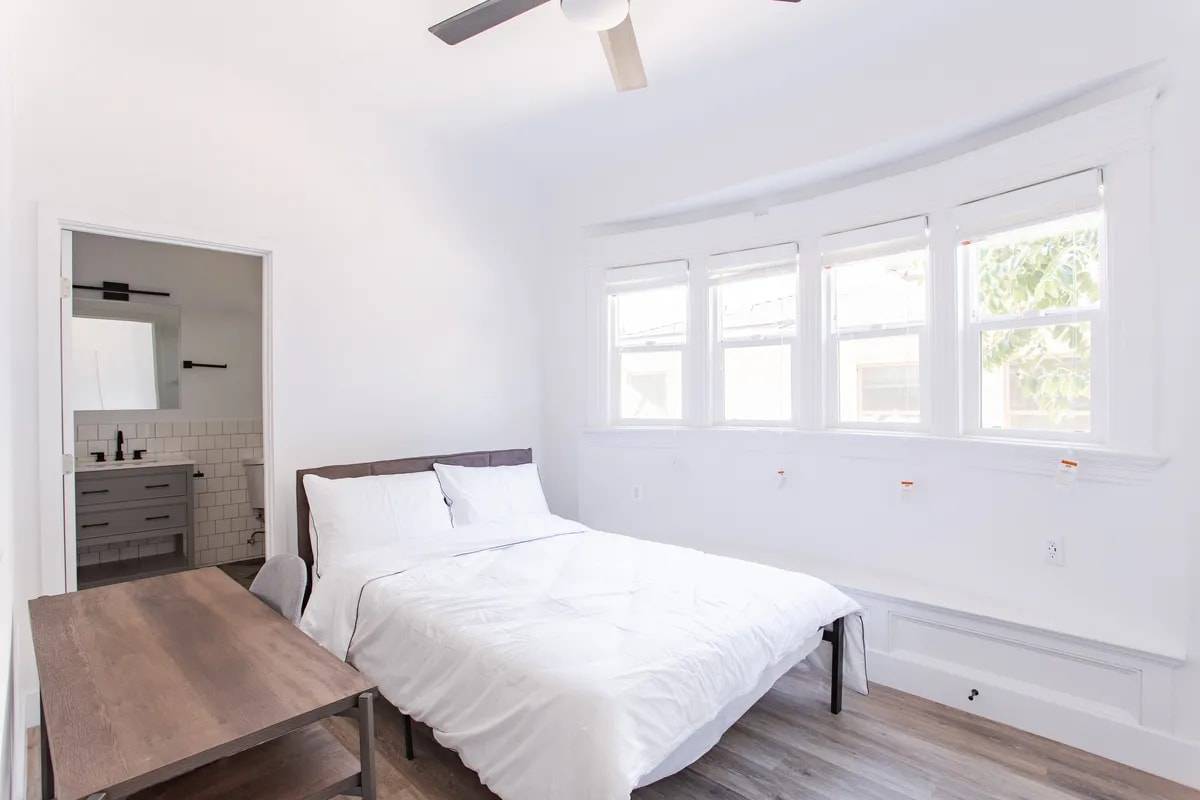 Bedroom with a curved bay of four windows and a built-in window seat, a bed and desk, and a door open to a private bathroom